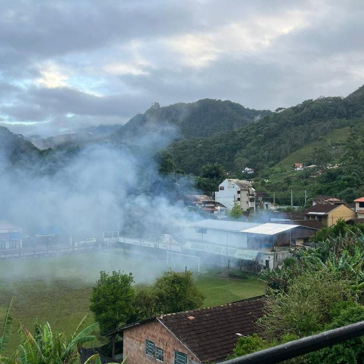 Incêndio na sede do Lumiar Futebol Clube em Nova Friburgo, com fumaça densa e montanhas ao fundo.