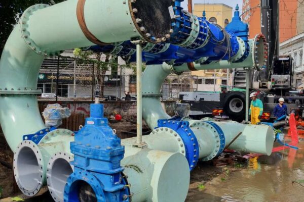 Instalação de tubulação em obra de saneamento, com trabalhadores e guindaste.