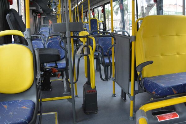 Interior de um ônibus com assentos amarelos e azuis, mostrando um aviso sobre a falta de direito a acento prioritário para pais de bebês.