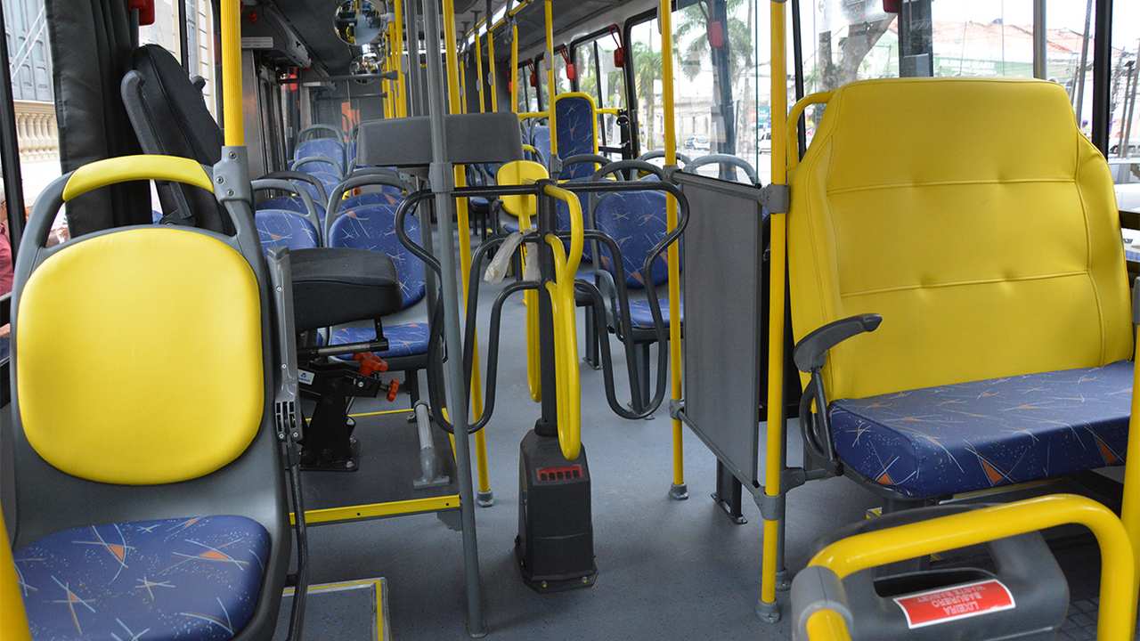 Interior de um ônibus com assentos amarelos e azuis, mostrando um aviso sobre a falta de direito a acento prioritário para pais de bebês.