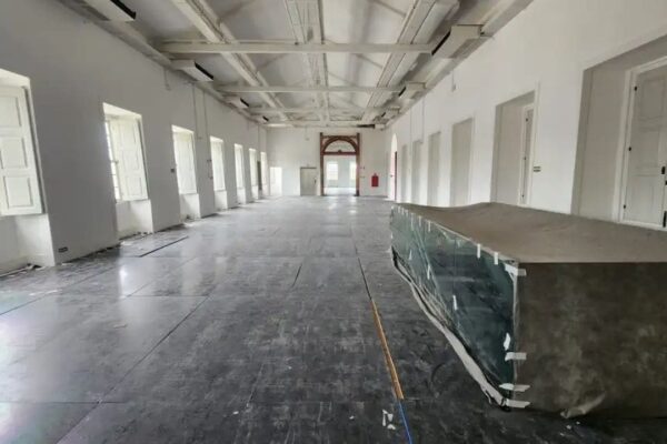 Interior do museu histórico com janelas, portas e objetos cobertos.