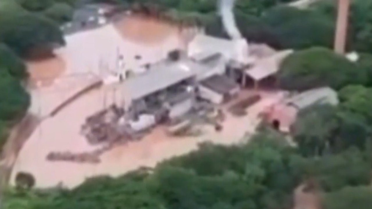 Inundação em área com prédios e vegetação, após rompimento de barragem.