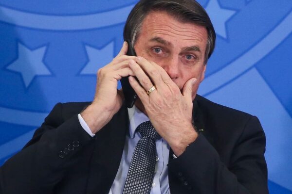 Jair Bolsonaro ao telefone, com expressão preocupada, possivelmente em conversa sobre tarifas de Trump.
