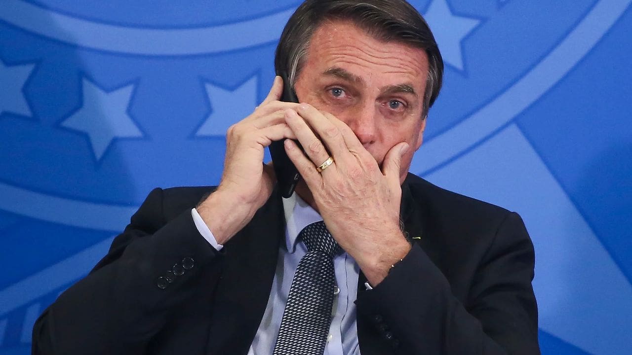 Jair Bolsonaro ao telefone, com expressão preocupada, possivelmente em conversa sobre tarifas de Trump.