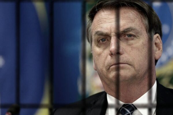Jair Bolsonaro atrás das grades, com o rosto sério, em referência à sua prisão domiciliar.
