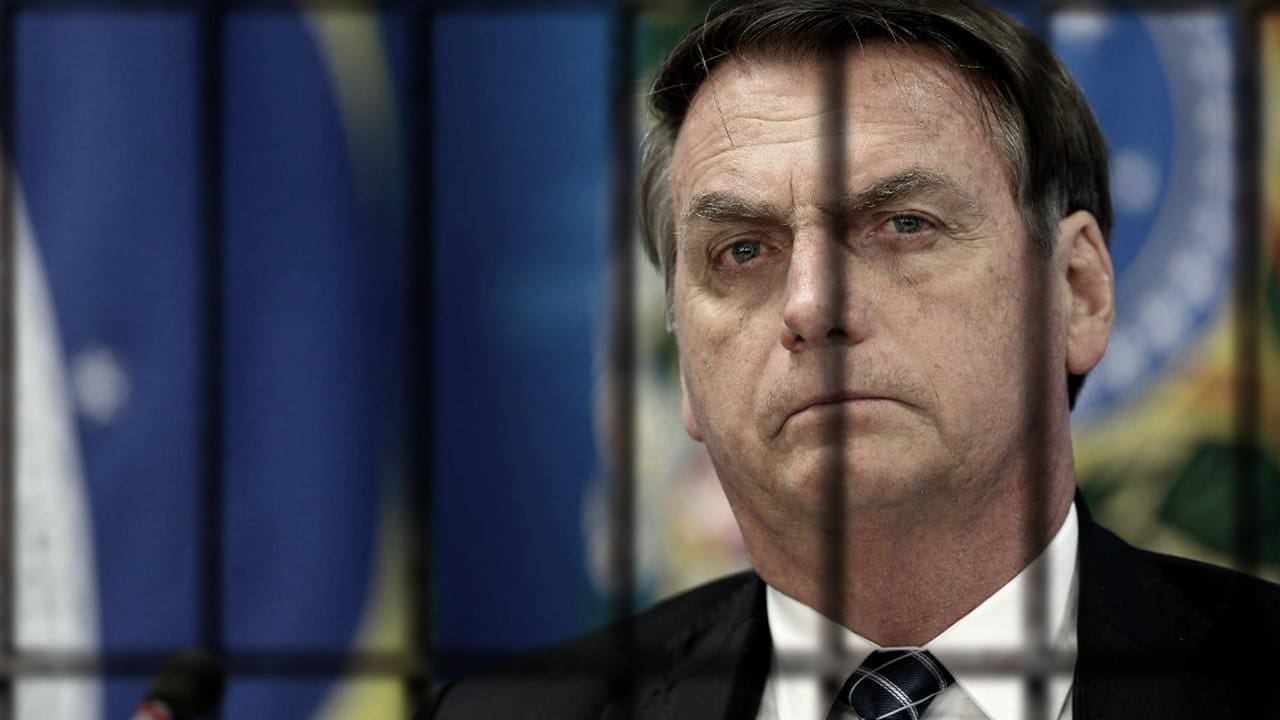 Jair Bolsonaro atrás das grades, com o rosto sério, em referência à sua prisão domiciliar.