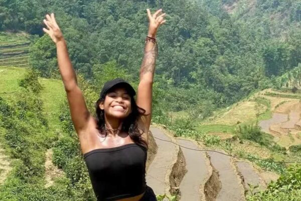 Juliana Marins, sorrindo, em uma paisagem montanhosa verde, com braços erguidos.