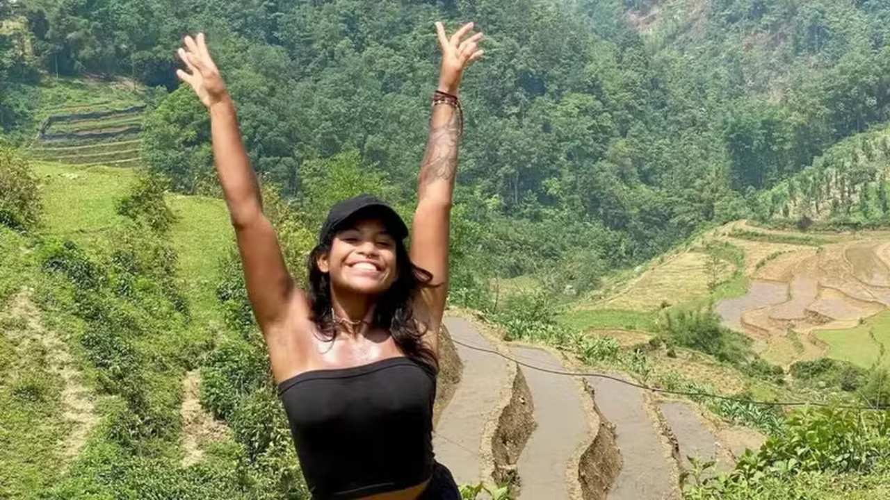 Juliana Marins, sorrindo, em uma paisagem montanhosa verde, com braços erguidos.
