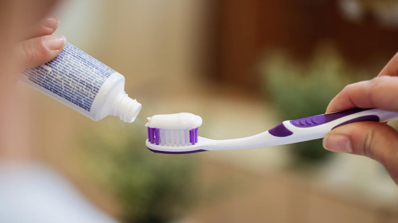 Mão apertando pasta de dente Colgate em uma escova de dentes