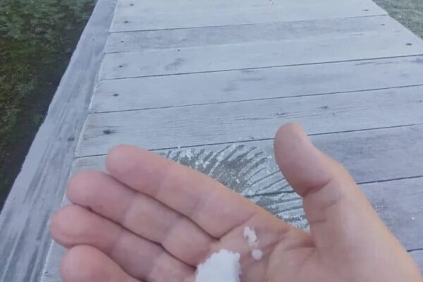 Mão segurando neve em um deck de madeira com geada, no Parque Estadual dos Três Picos.