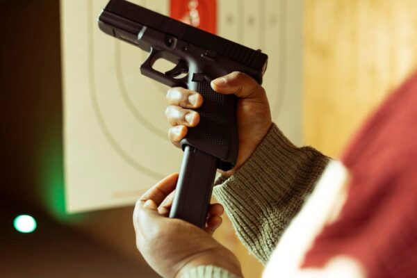 Mãos segurando uma pistola preta e carregador em um ambiente de tiro.
