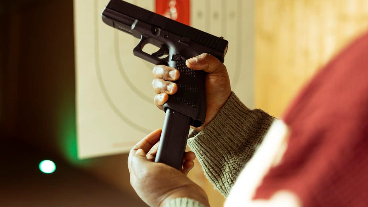 Mãos segurando uma pistola preta e carregador em um ambiente de tiro.