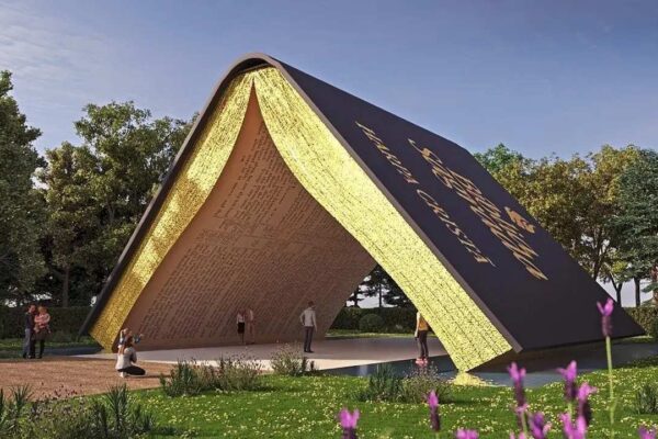 Monumento gigante em forma de livro aberto no centro de um jardim, com pessoas em volta