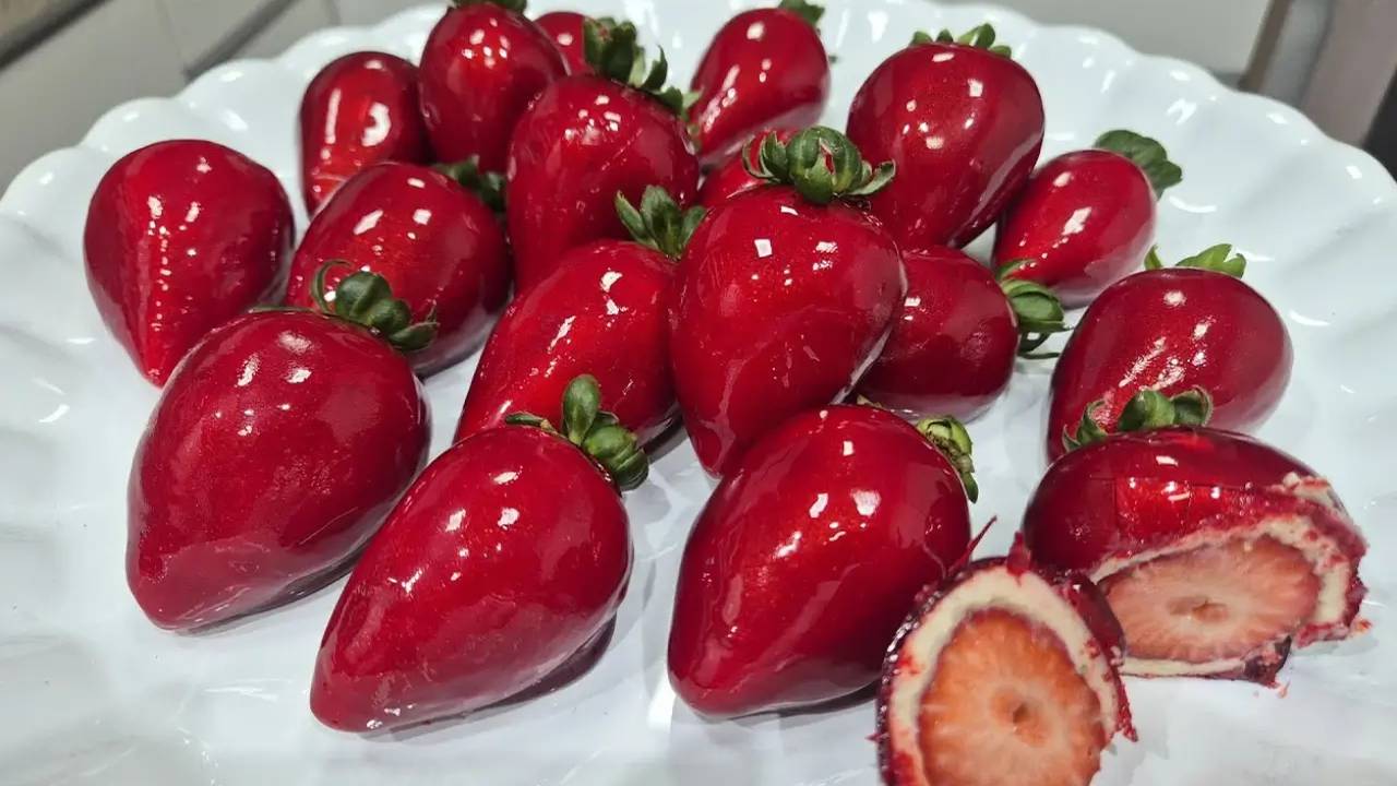 Morango do Amor brilhante em prato branco, com um cortado mostrando o interior.