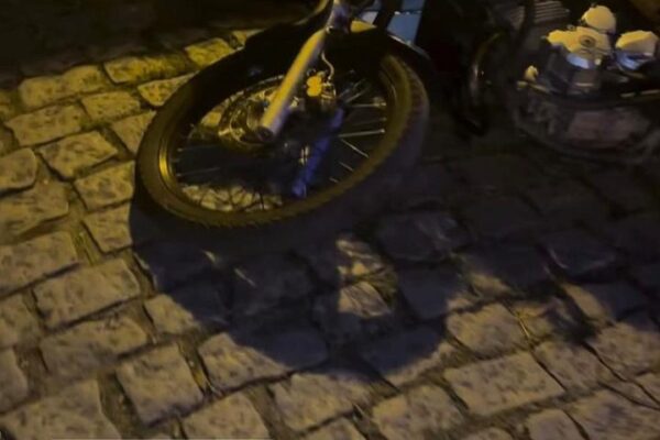 Motocicleta em calçada de paralelepípedos, com texto sobre violência policial.
