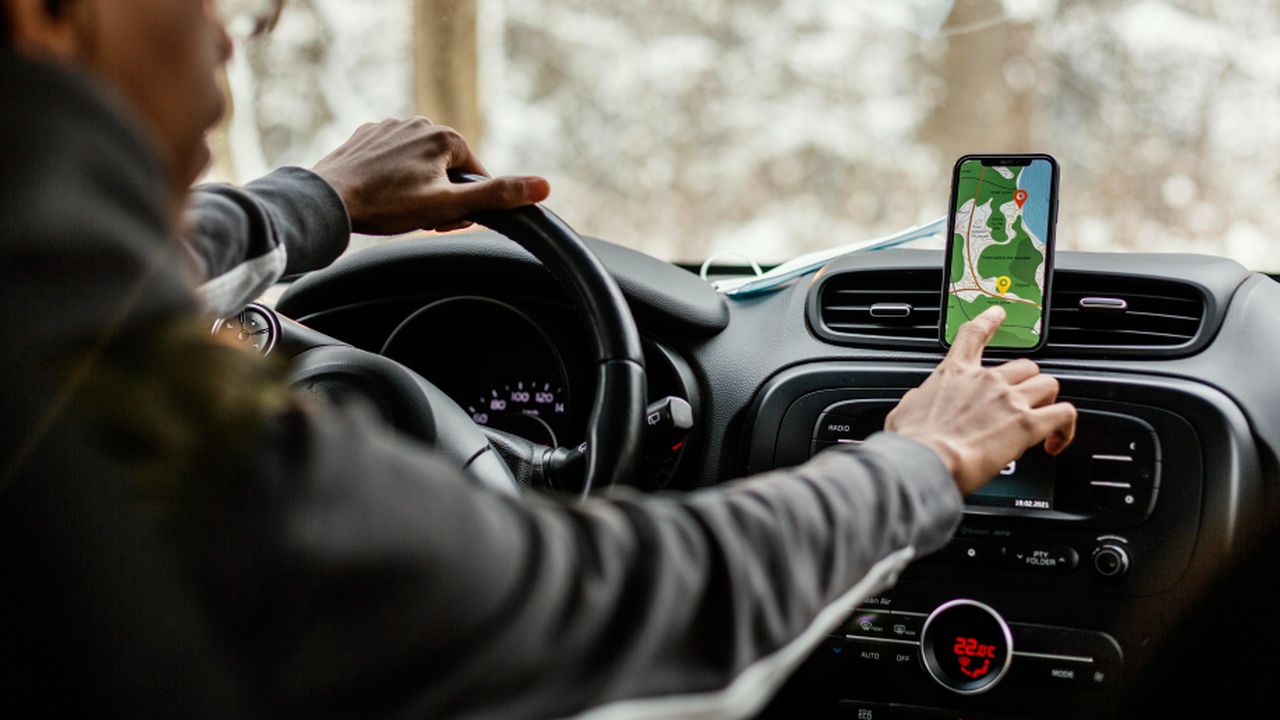 Motorista usando aplicativo de GPS em um carro, com mapa aberto no celular.