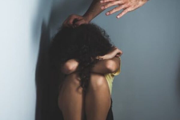 Mulher encolhida com mãos pairando acima, simbolizando violência doméstica.