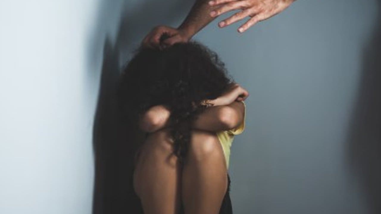 Mulher encolhida com mãos pairando acima, simbolizando violência doméstica.