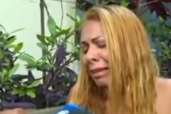 Mulher loira chora, possivelmente em choque, com plantas ao fundo.