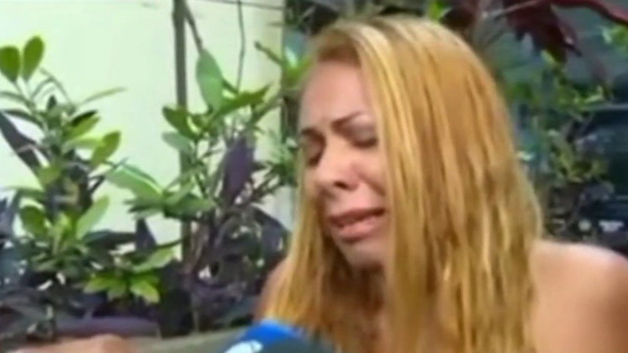 Mulher loira chora, possivelmente em choque, com plantas ao fundo.
