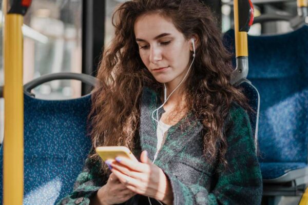 Mulher no ônibus usando fones de ouvido e celular.
