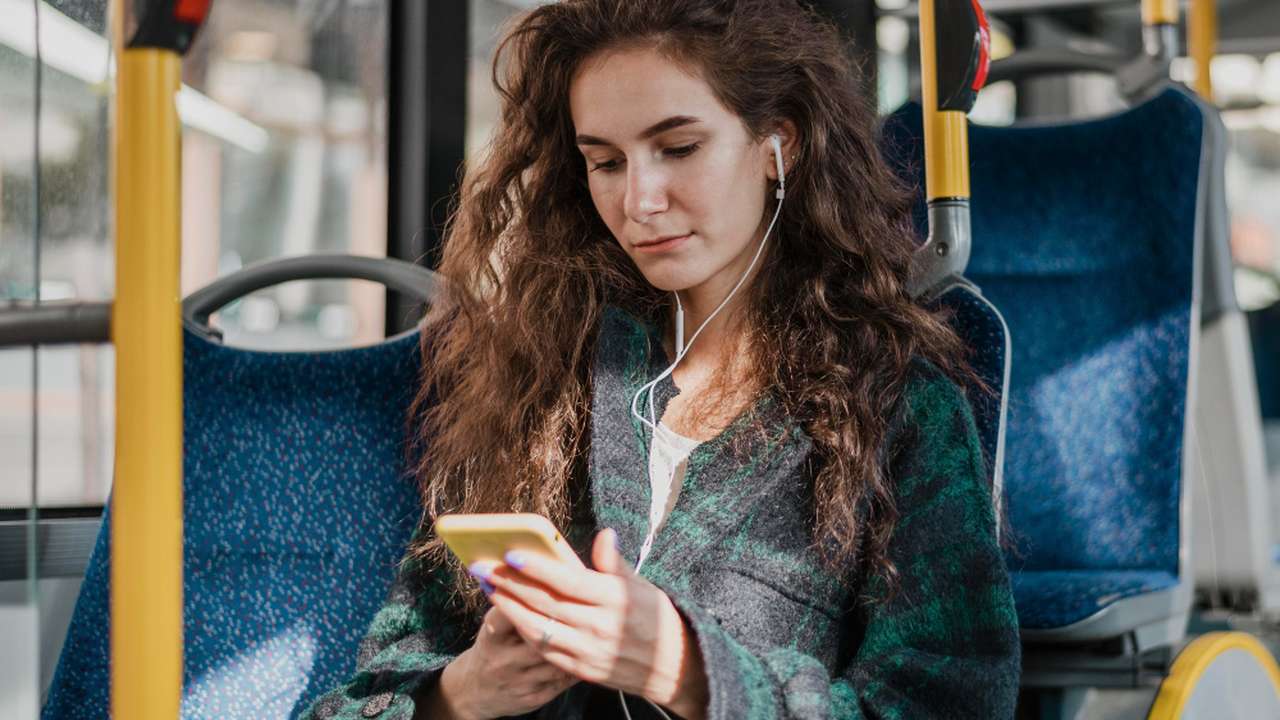 Mulher no ônibus usando fones de ouvido e celular.