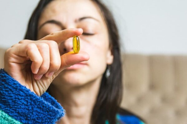 Mulher segura cápsula de vitamina, em alusão à proibição de marcas de suplementos no Brasil.