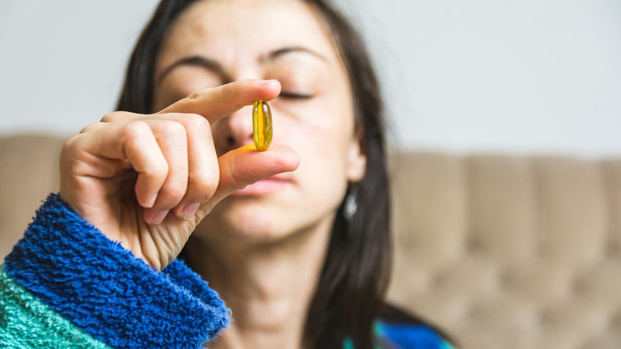 Mulher segura cápsula de vitamina, em alusão à proibição de marcas de suplementos no Brasil.