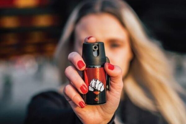 Mulher segura spray de defesa pessoal com unhas vermelhas em destaque.