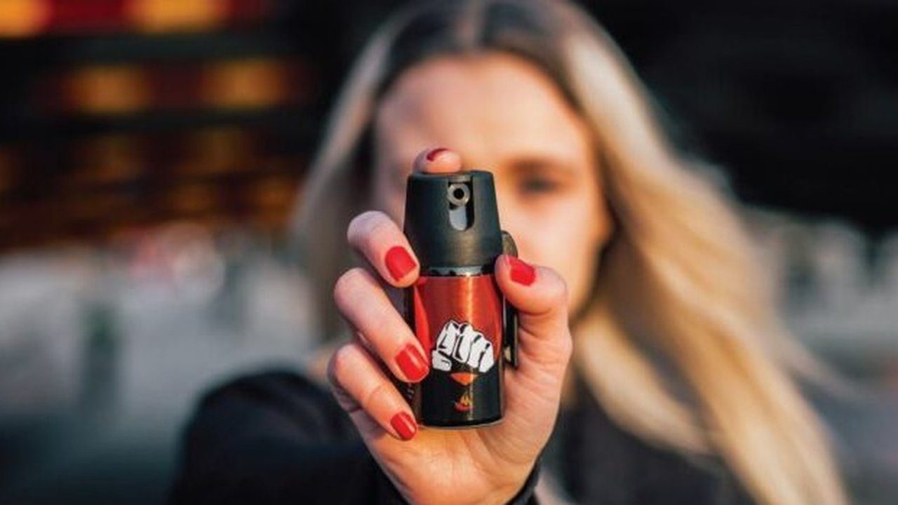 Mulher segura spray de defesa pessoal com unhas vermelhas em destaque.