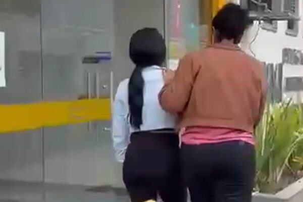 Mulher sendo detida por agentes da lei em frente a um prédio.