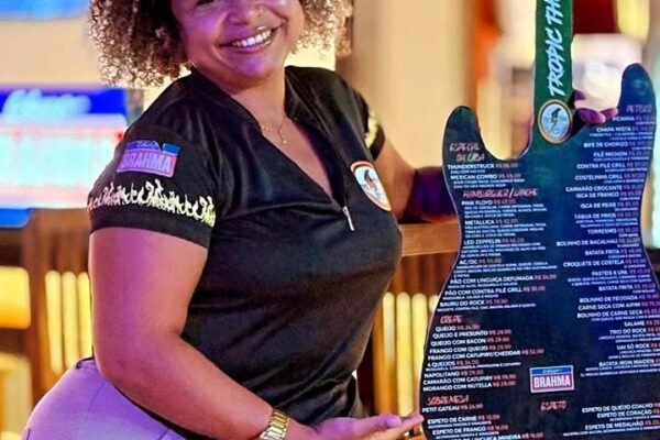 Mulher sorrindo segura cardápio de restaurante 'Tropic Thunder Rock' em formato de guitarra.