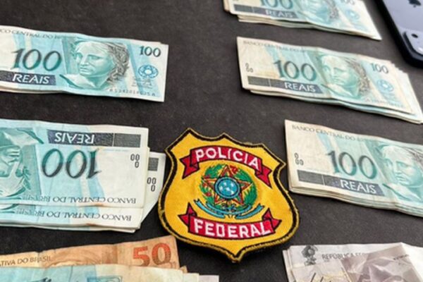 Notas de dinheiro e distintivo da Polícia Federal em apreensão.