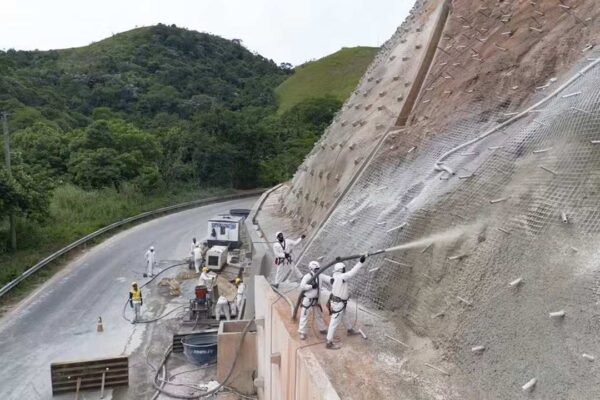 Obras na RJ-127: aplicação de concreto em encosta, com trabalhadores utilizando equipamentos de segurança.