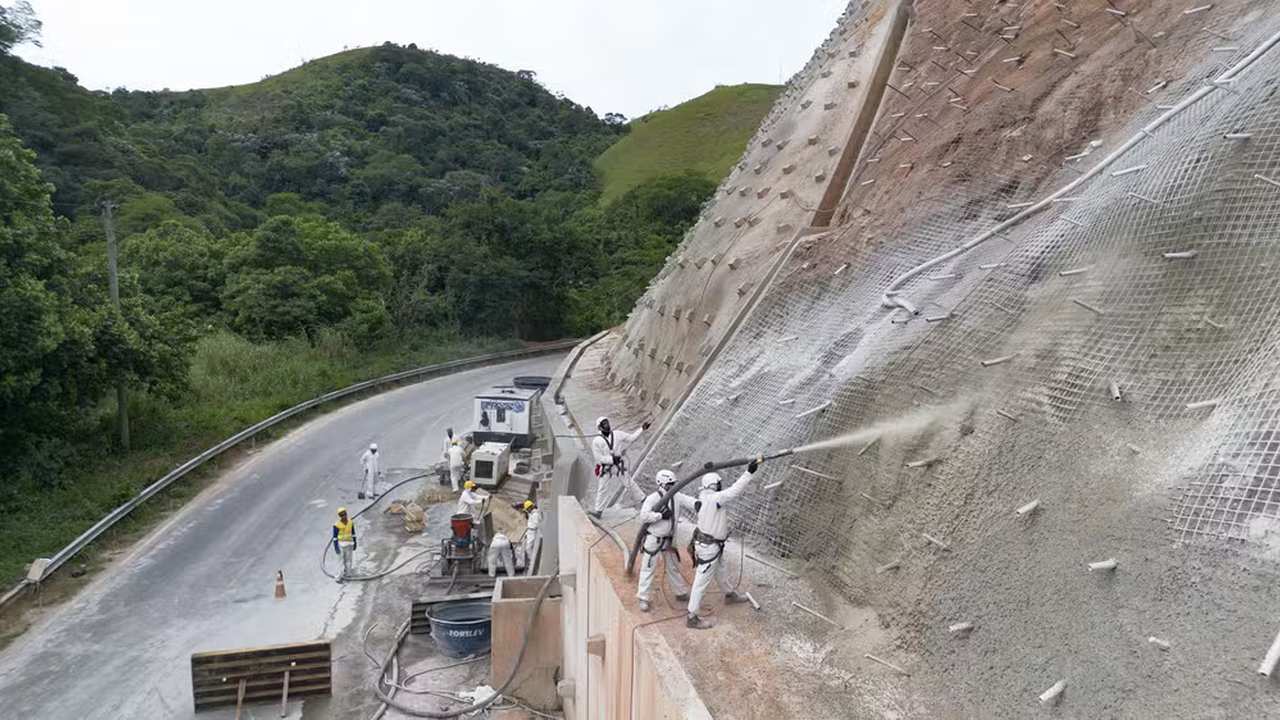 Obras na RJ-127: aplicação de concreto em encosta, com trabalhadores utilizando equipamentos de segurança.