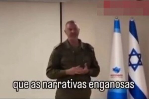 Oficial israelense em apresentação sobre narrativas enganosas, com bandeiras de Israel ao fundo.