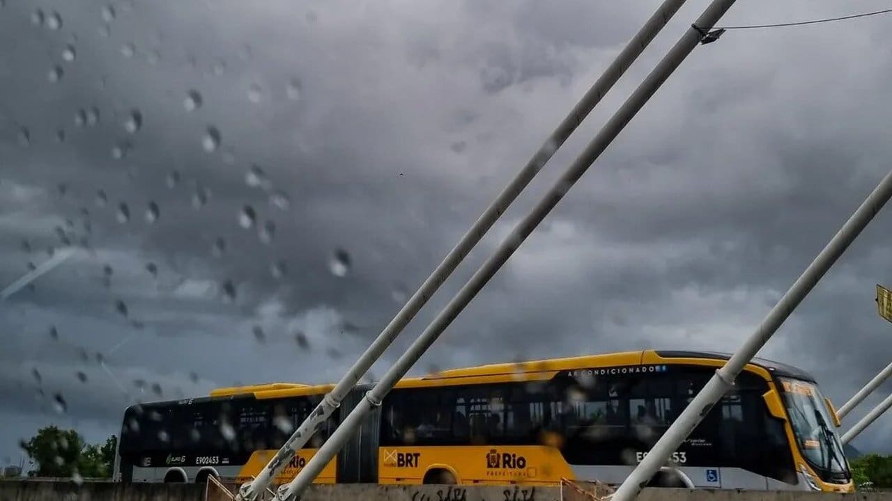 Ônibus amarelo em uma parada de ônibus, com chuva caindo e céu nublado.
