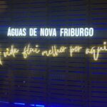 Painel de madeira com letreiro luminoso 'Águas de Nova Friburgo' e a frase 'A vida flui melhor por aqui'.