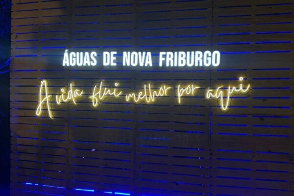 Painel de madeira com letreiro luminoso 'Águas de Nova Friburgo' e a frase 'A vida flui melhor por aqui'.