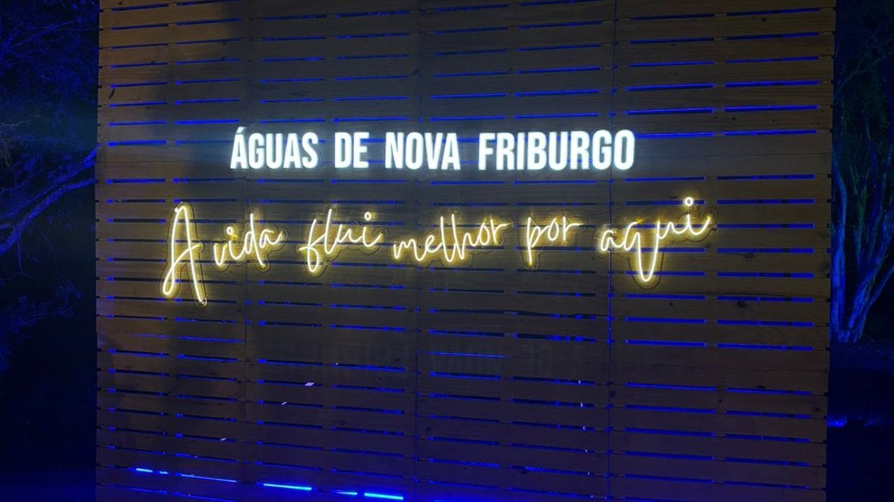 Painel de madeira com letreiro luminoso 'Águas de Nova Friburgo' e a frase 'A vida flui melhor por aqui'.