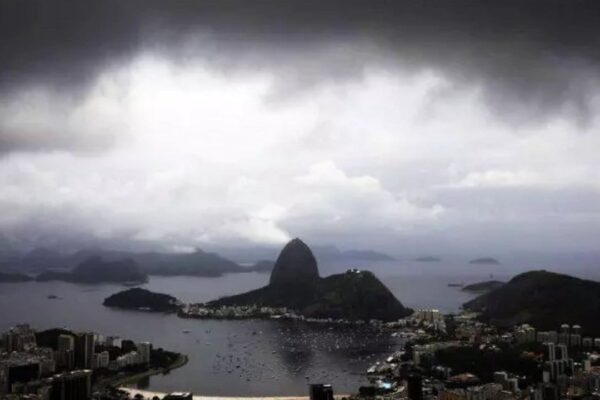 Paisagem chuvosa no Rio de Janeiro com montanhas e a Baía de Guanabara sob céu nublado.