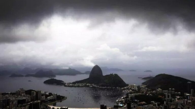 Paisagem chuvosa no Rio de Janeiro com montanhas e a Baía de Guanabara sob céu nublado.