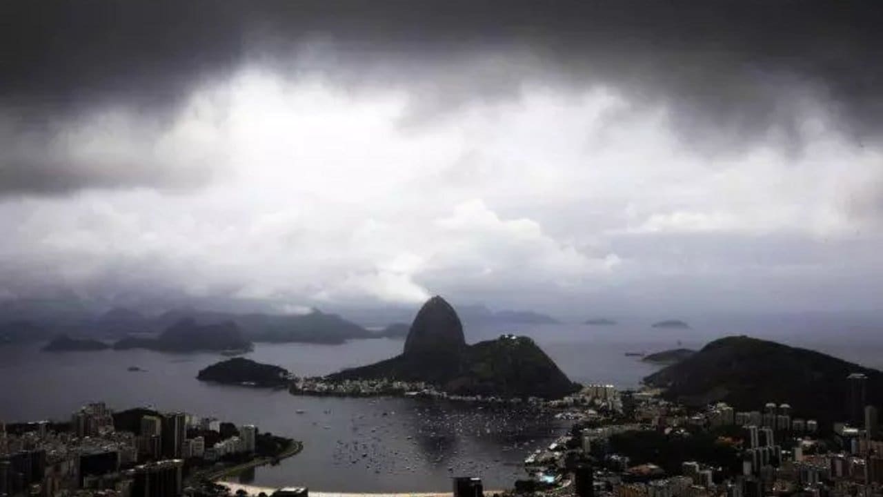 Paisagem chuvosa no Rio de Janeiro com montanhas e a Baía de Guanabara sob céu nublado.