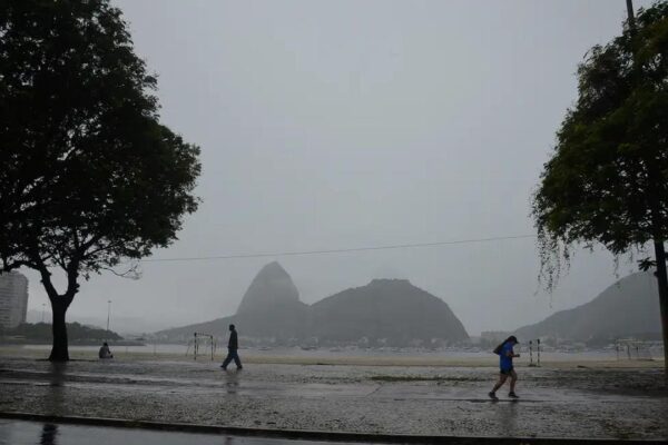 Paisagem chuvosa no Rio de Janeiro com pessoas caminhando e montanhas ao fundo.