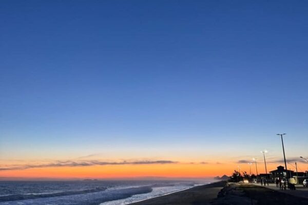 Paisagem da praia de Maricá ao entardecer, com céu azul e lua crescente
