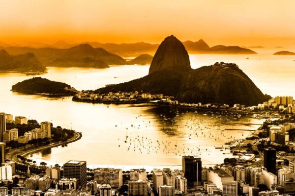 Paisagem do Rio de Janeiro com montanhas, baía e cidade ao pôr do sol.