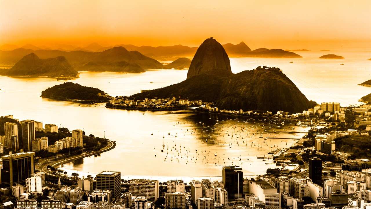 Paisagem do Rio de Janeiro com montanhas, baía e cidade ao pôr do sol.