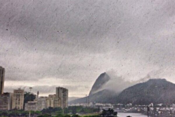 Paisagem urbana do Rio de Janeiro com montanhas e céu nublado. Predominância de prédios e vegetação.