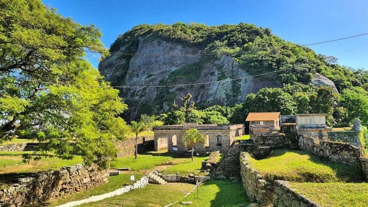Parque Histórico Monte Bastione em Niterói com ruínas, vegetação exuberante e vista da montanha.