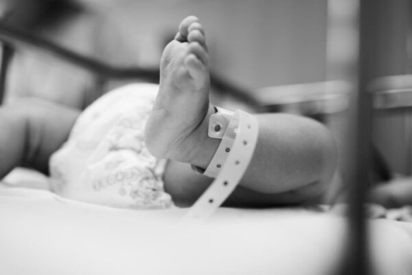 Pé de bebê com pulseira de identificação em berço de hospital.